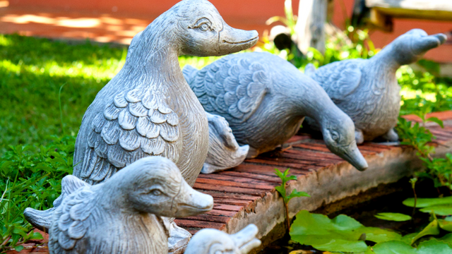 Duck statues resting on the side of as pond.