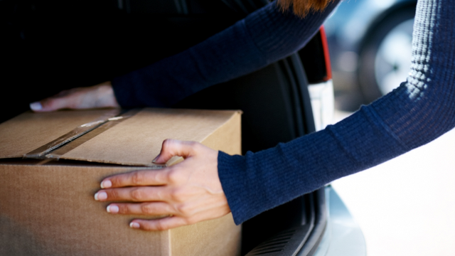 A cardboard box being placed into a trunk.