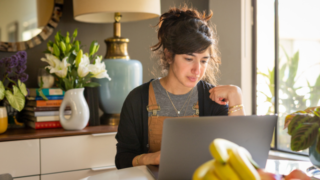 A woman typing on a laptop, surrounded by plants.